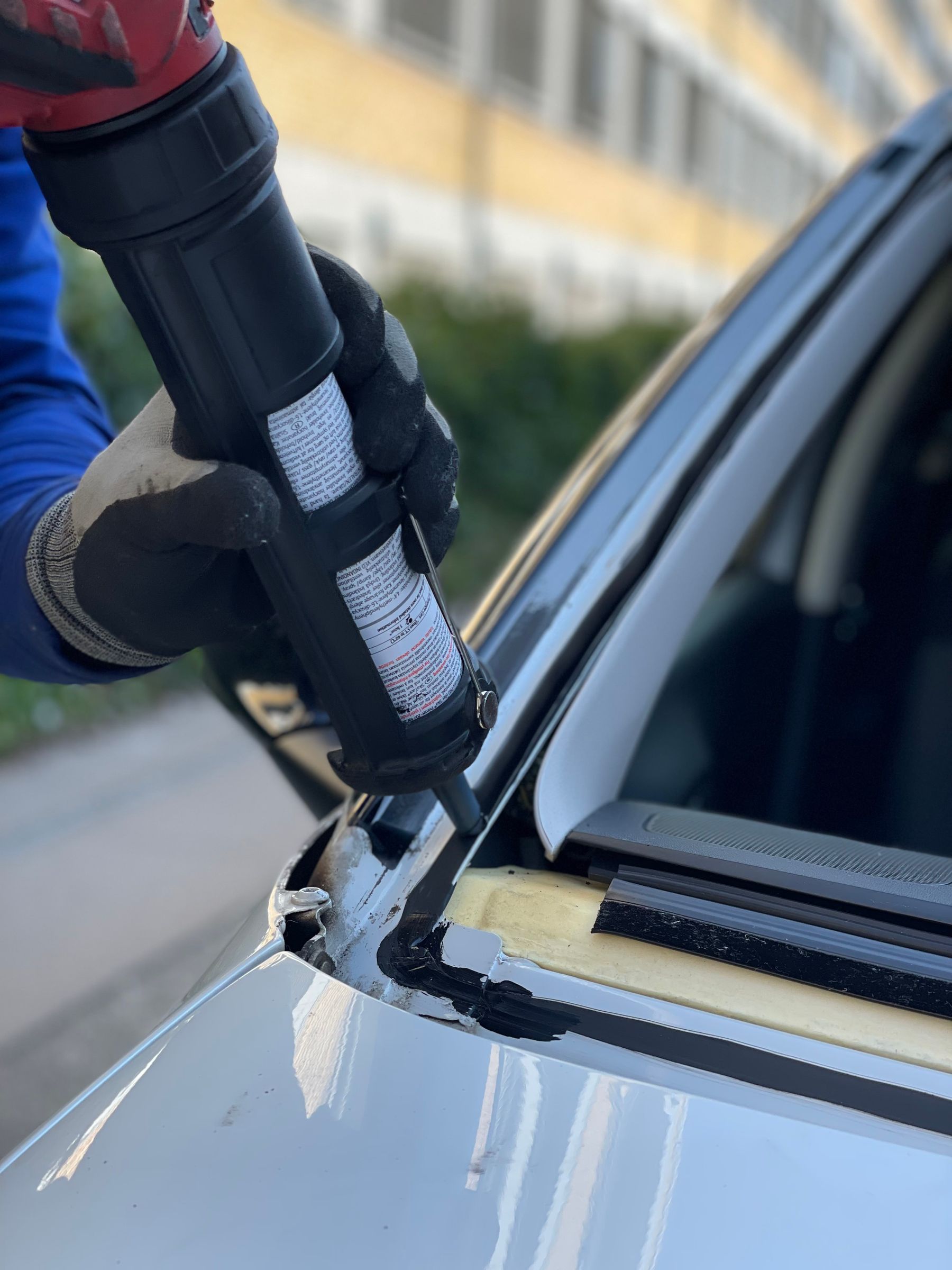 Gloved technician applying adhesive to a vehicle’s windshield opening